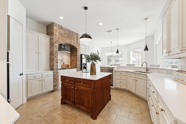 kitchen with appliances with stainless steel finishes, wall chimney exhaust hood, sink, pendant lighting, and an island with sink