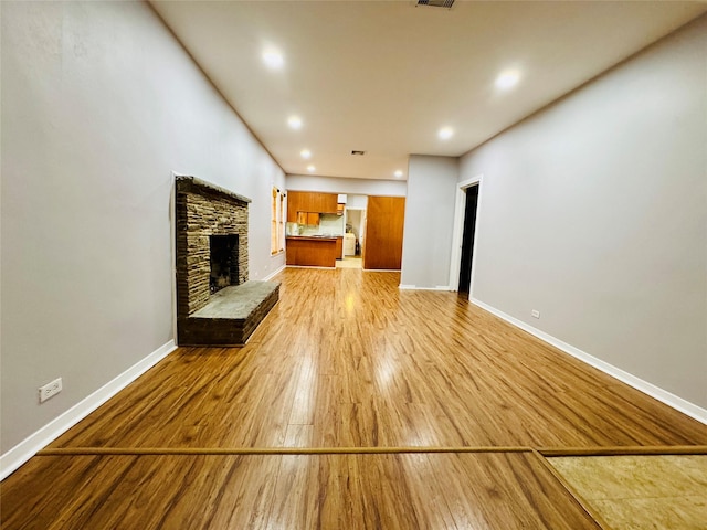 unfurnished living room with a stone fireplace and light hardwood / wood-style floors