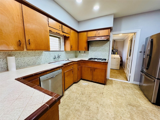 kitchen featuring backsplash, stainless steel appliances, sink, washer / dryer, and tile counters