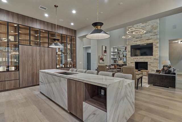 kitchen with a stone fireplace, light stone countertops, sink, and light hardwood / wood-style flooring