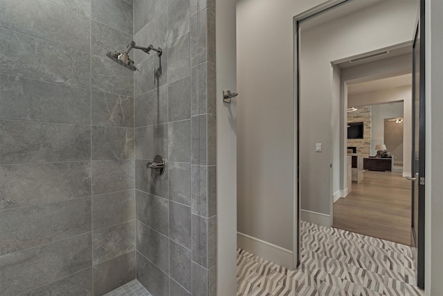 bathroom with a stone fireplace, hardwood / wood-style floors, and tiled shower