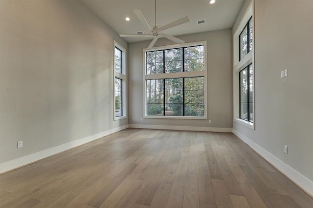 unfurnished room with plenty of natural light, a towering ceiling, and light hardwood / wood-style flooring