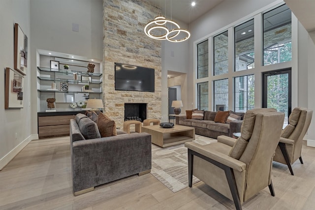 living room with a chandelier, a fireplace, a towering ceiling, and light hardwood / wood-style floors