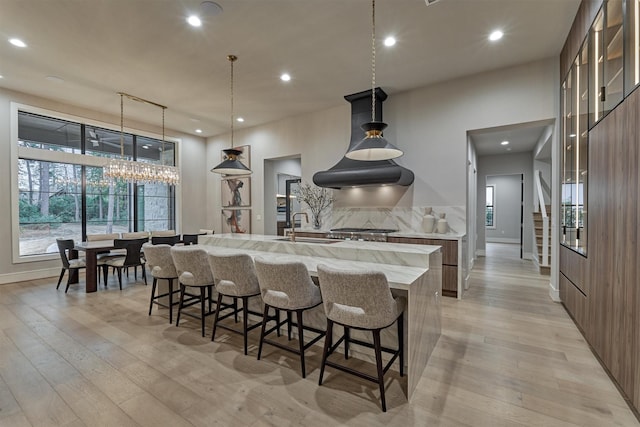 kitchen featuring pendant lighting, a large island with sink, a kitchen breakfast bar, sink, and light hardwood / wood-style flooring