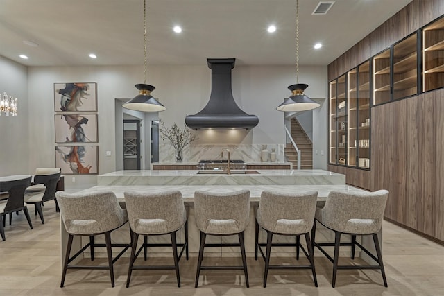 kitchen with decorative light fixtures, backsplash, light hardwood / wood-style floors, and range hood