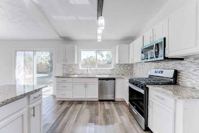 kitchen featuring white cabinetry, hanging light fixtures, appliances with stainless steel finishes, and light hardwood / wood-style flooring