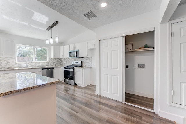 kitchen with hanging light fixtures, light hardwood / wood-style flooring, appliances with stainless steel finishes, light stone counters, and white cabinetry