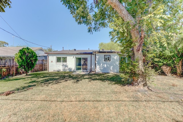 rear view of property featuring solar panels and a yard