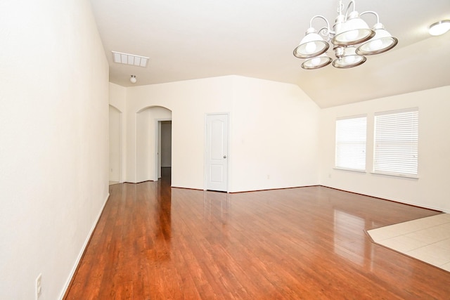 spare room with vaulted ceiling, dark hardwood / wood-style floors, and an inviting chandelier