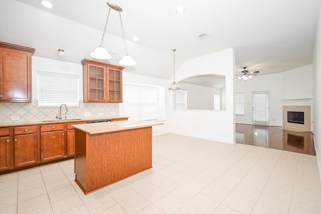 kitchen with a tile fireplace, ceiling fan, backsplash, pendant lighting, and a kitchen island