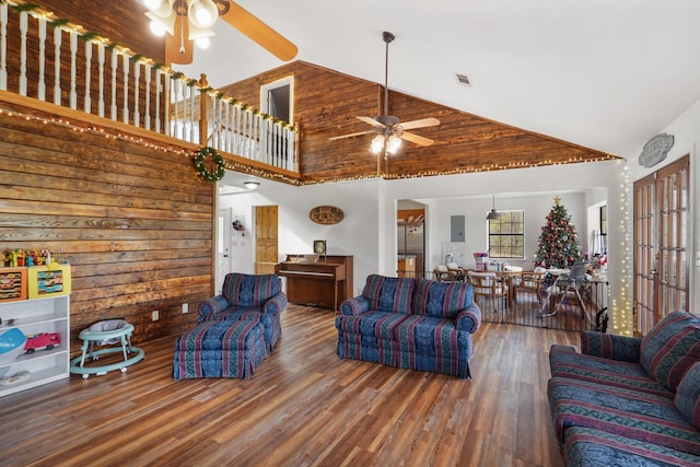 living room with wooden walls, ceiling fan, dark wood-type flooring, and high vaulted ceiling