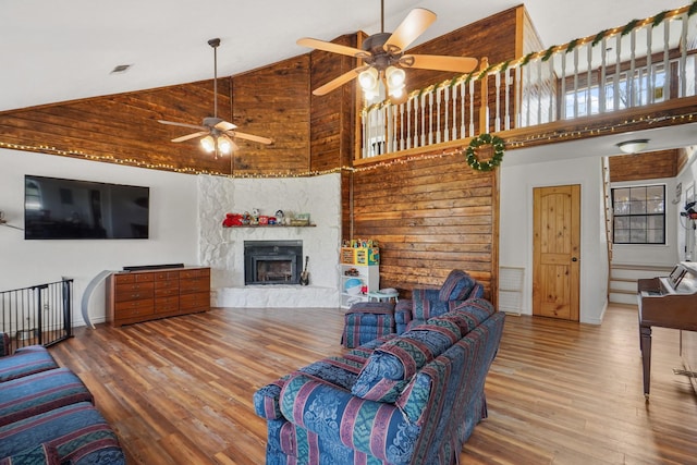 living room featuring wood-type flooring, high vaulted ceiling, a stone fireplace, and ceiling fan