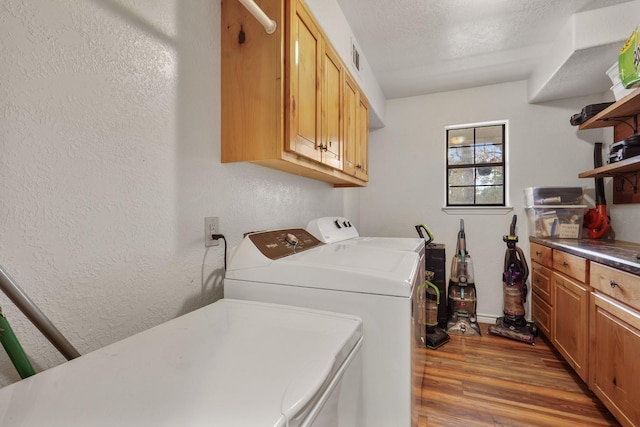 clothes washing area featuring cabinets, washing machine and dryer, a textured ceiling, and light hardwood / wood-style flooring