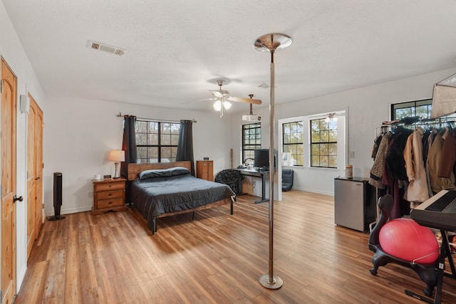 bedroom featuring a textured ceiling, light hardwood / wood-style floors, fridge, and ceiling fan