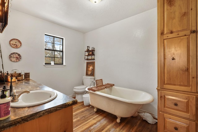 bathroom with a bath, vanity, wood-type flooring, and toilet