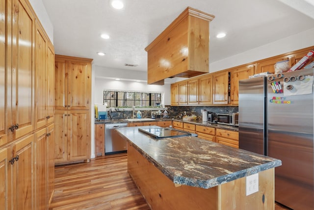 kitchen with stainless steel appliances, backsplash, dark stone counters, light hardwood / wood-style floors, and a kitchen island