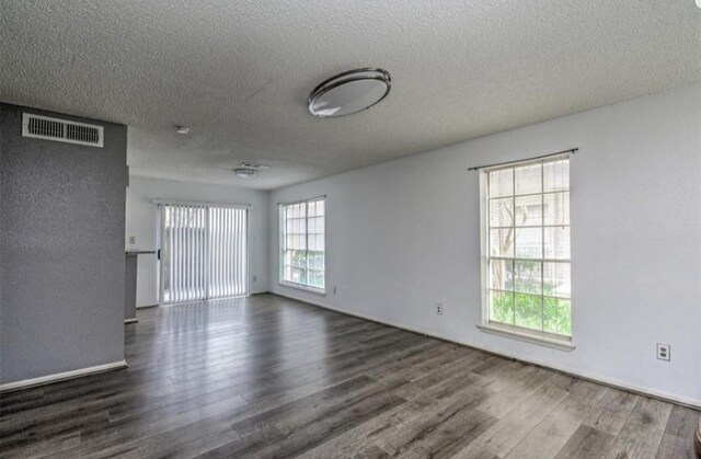 empty room with dark hardwood / wood-style flooring, a textured ceiling, and a wealth of natural light