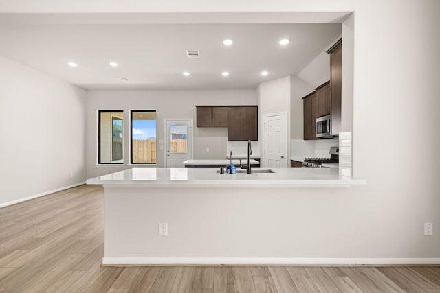 kitchen with sink, kitchen peninsula, light hardwood / wood-style floors, dark brown cabinets, and appliances with stainless steel finishes