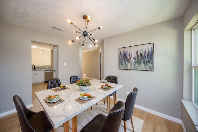 dining space with light hardwood / wood-style floors, sink, a textured ceiling, and a chandelier