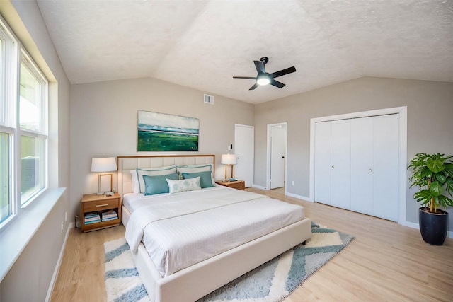 bedroom featuring ceiling fan, a textured ceiling, lofted ceiling, a closet, and light wood-type flooring