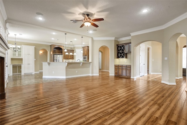 unfurnished living room featuring ceiling fan with notable chandelier, dark wood-type flooring, a textured ceiling, and ornamental molding