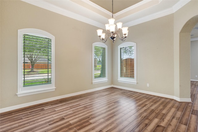 empty room featuring wood-type flooring, crown molding, a tray ceiling, and a chandelier