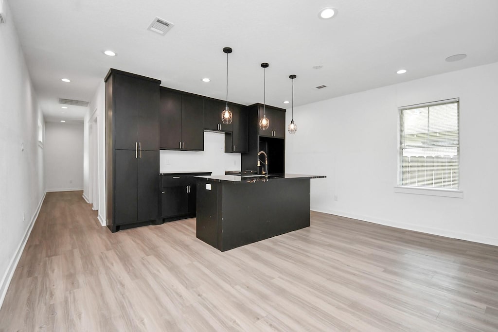 kitchen featuring a center island with sink, sink, hanging light fixtures, and light hardwood / wood-style flooring