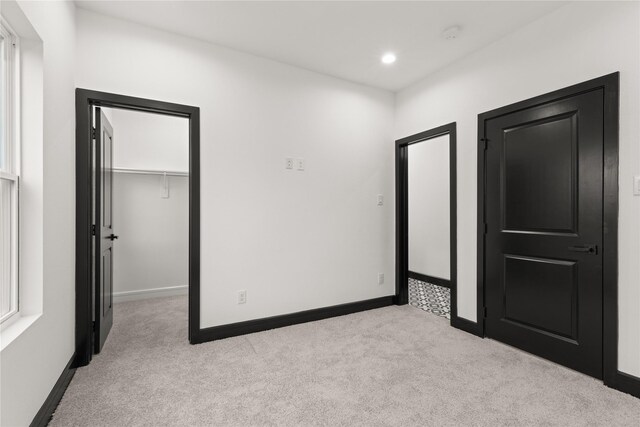 unfurnished bedroom with a walk in closet, light carpet, and a closet