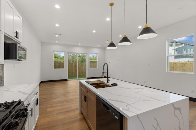 kitchen featuring light stone counters, a center island with sink, white cabinetry, and black appliances