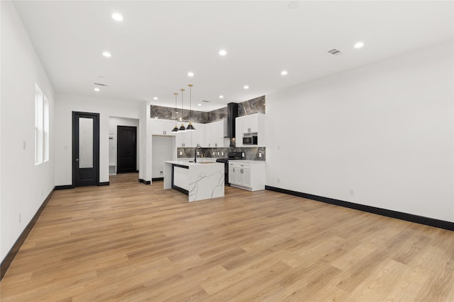 kitchen featuring light wood-type flooring, stainless steel appliances, decorative light fixtures, white cabinets, and a kitchen island