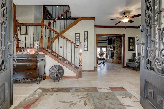 foyer entrance featuring a stone fireplace, ceiling fan, and crown molding