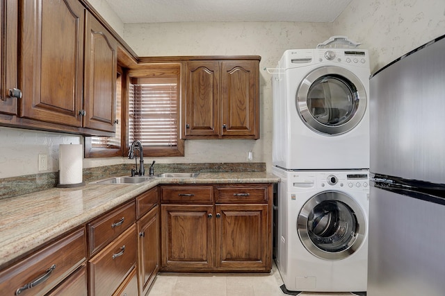 clothes washing area featuring sink, cabinets, a textured ceiling, light tile patterned flooring, and stacked washer and clothes dryer