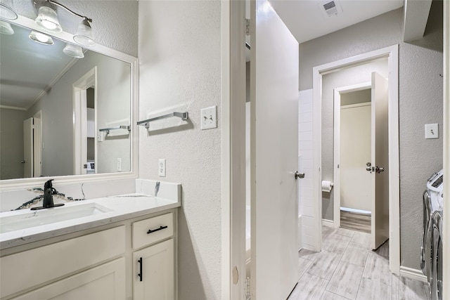 bathroom with washer and dryer, vanity, and crown molding