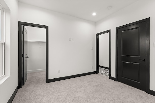 unfurnished bedroom featuring a walk in closet, light carpet, and a closet