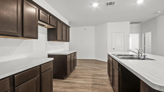 kitchen with a center island with sink, dark brown cabinets, wood-type flooring, and sink