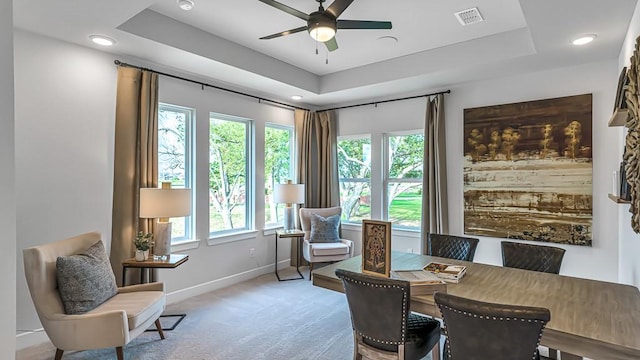 dining space featuring light carpet, a tray ceiling, ceiling fan, and a healthy amount of sunlight