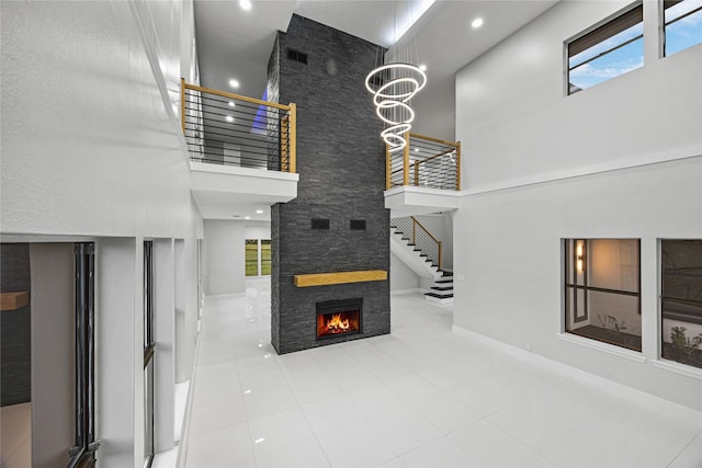 living room with a stone fireplace, tile patterned flooring, a towering ceiling, and a chandelier