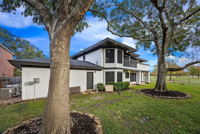 rear view of house featuring a yard, a balcony, and central AC unit