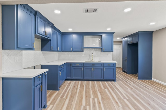 kitchen featuring backsplash, light hardwood / wood-style floors, blue cabinets, and sink