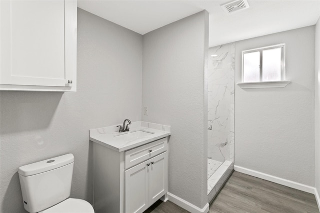 bathroom with a tile shower, toilet, vanity, and hardwood / wood-style flooring