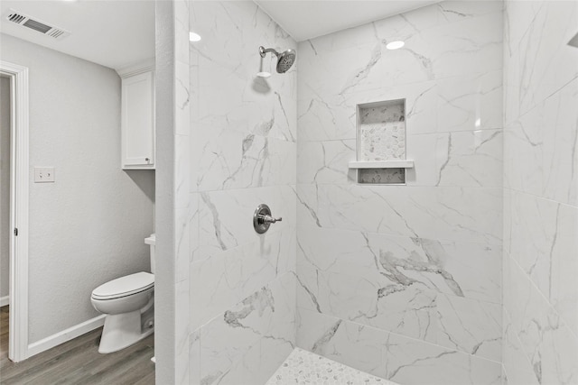 bathroom featuring toilet, wood-type flooring, and tiled shower