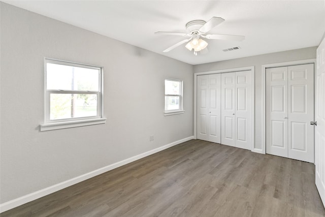 unfurnished bedroom featuring multiple closets, ceiling fan, and hardwood / wood-style floors