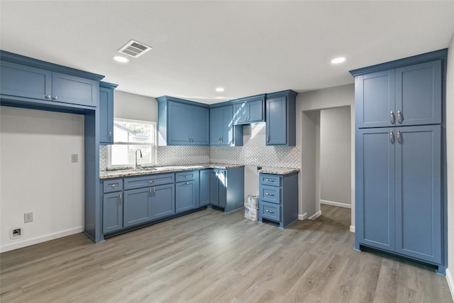 kitchen featuring decorative backsplash, light wood-type flooring, light stone counters, sink, and blue cabinetry