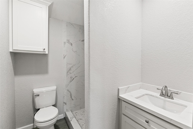 bathroom with vanity, toilet, and tiled shower