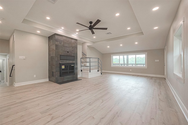 unfurnished living room featuring light hardwood / wood-style floors, ceiling fan, a tray ceiling, and a tiled fireplace