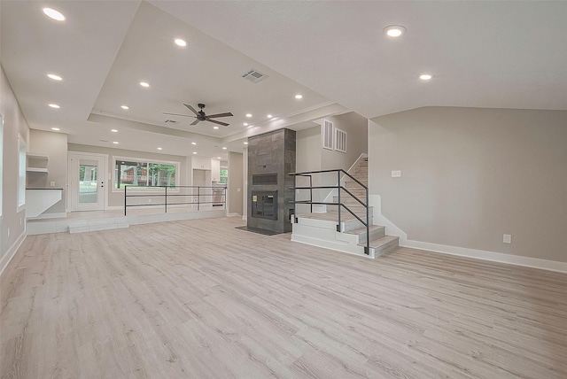 unfurnished living room with ceiling fan, light wood-type flooring, a tile fireplace, and vaulted ceiling