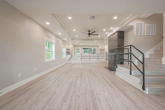 unfurnished living room with ceiling fan, a raised ceiling, and light hardwood / wood-style flooring