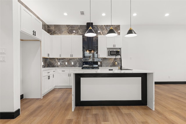 kitchen with a kitchen island with sink, hanging light fixtures, light hardwood / wood-style flooring, gas stove, and white cabinetry