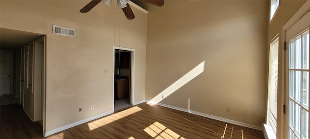 empty room with ceiling fan, dark hardwood / wood-style flooring, and a towering ceiling