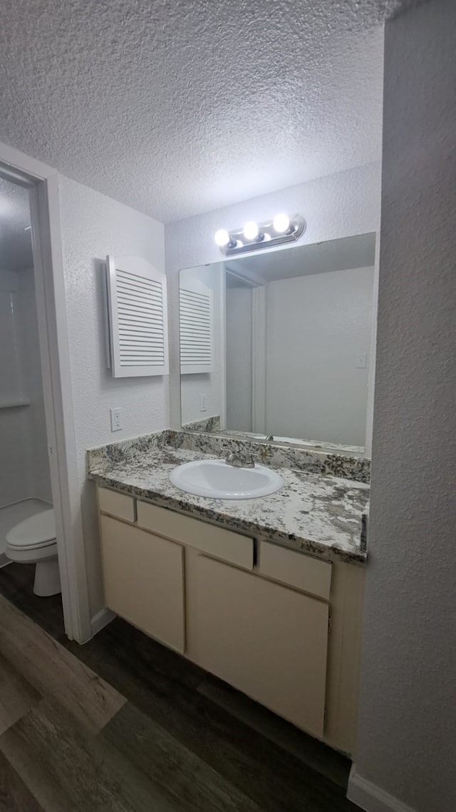 bathroom with hardwood / wood-style floors, vanity, a shower, toilet, and a textured ceiling